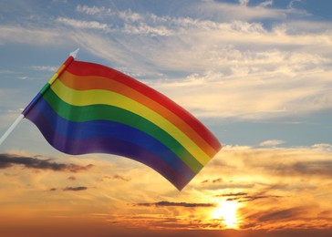 Bright rainbow LGBT flag against sky at sunset