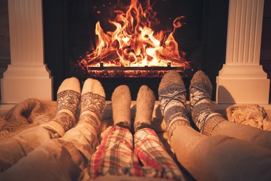 Lovely family in warm socks resting near fireplace at home, closeup