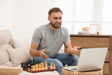 Photo of Young man playing chess with partner through online video chat at home