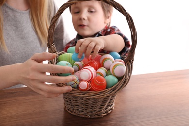 Little boy and his mother with basket full of dyed Easter eggs at wooden table, closeup. Easter celebration
