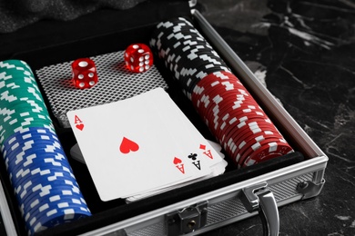 Gaming chips, dices and cards in suitcase on dark marble table