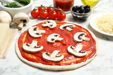 Pizza crust with tomato sauce, mushrooms and ingredients on marble table