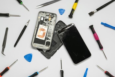 Damaged smartphone and repair tool set on white background, flat lay
