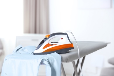 Modern electric iron and clean shirt on board indoors