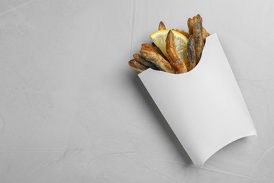Photo of Paper bag with delicious fried anchovies and lemon slice on light table, top view. Space for text