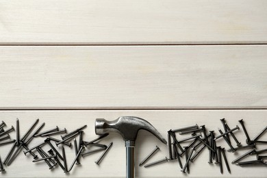 Photo of Hammer and metal nails on white wooden table, flat lay. Space for text