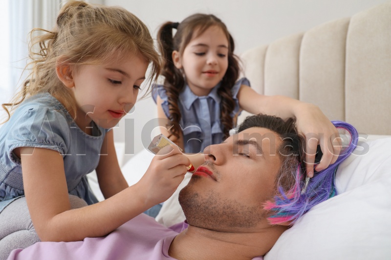 Cute little children painting face of their father while he sleeping in bed at home
