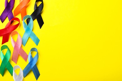 Colorful ribbons on yellow background, flat lay with space for text. World Cancer Day