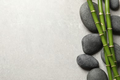 Spa stones and bamboo stems on light grey table, flat lay. Space for text
