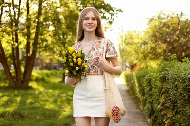 Beautiful teenage girl with bouquet of yellow tulips and apples in park on sunny day