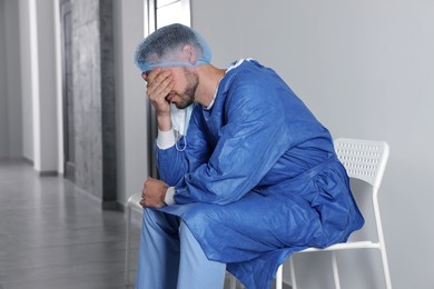 Photo of Exhausted doctor sitting on chair in hospital corridor