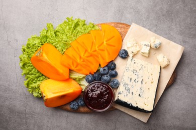 Photo of Delicious persimmon, blue cheese, blueberries and jam served on light grey table, flat lay