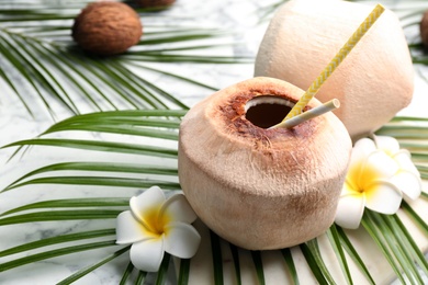 Fresh coconut with drinking straws and flowers on white marble table, closeup