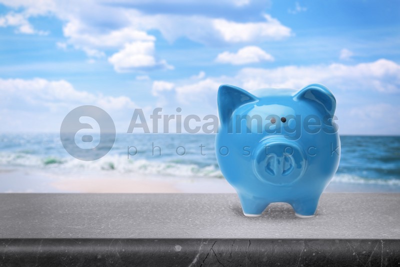 Saving money for summer vacation. Piggy bank on stone surface near sea, space for text