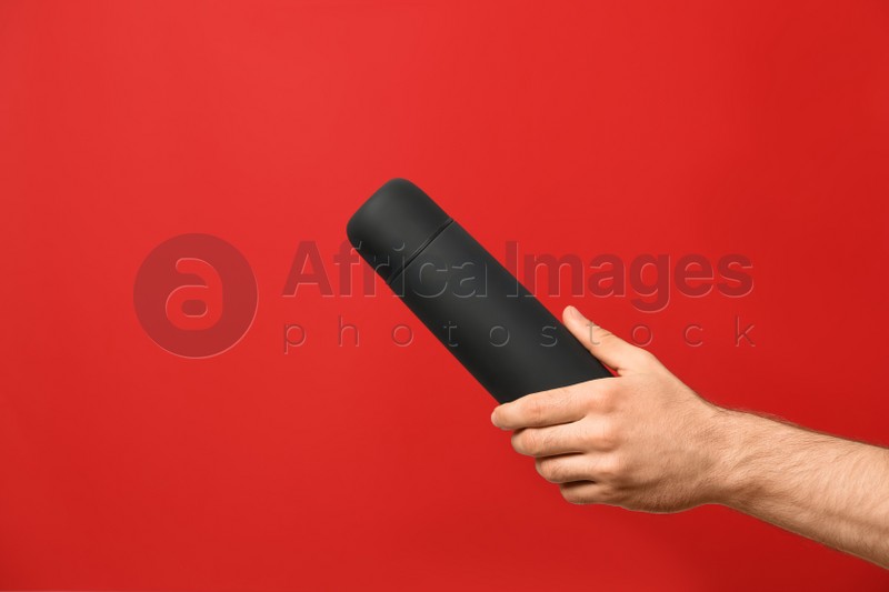 Man holding black thermos on red background, closeup
