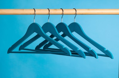 Bright clothes hangers on wooden rail against light blue background