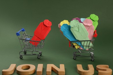 Photo of Recruitment process, job competition concept. Composition with phrase Join Us, paper human figures and toy shopping carts on green background