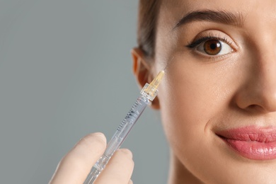 Beautiful woman getting facial injection on grey background, closeup. Cosmetic surgery