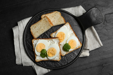 Tasty sandwiches with boiled eggs served on black table, flat lay
