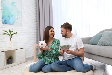Photo of Beautiful young couple with piggy bank and money at home