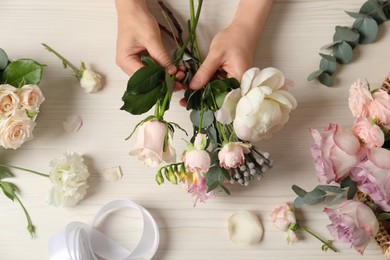 Florist creating beautiful bouquet at white table, top view