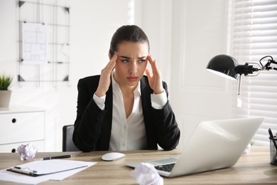 Stressed and tired young woman with headache at workplace