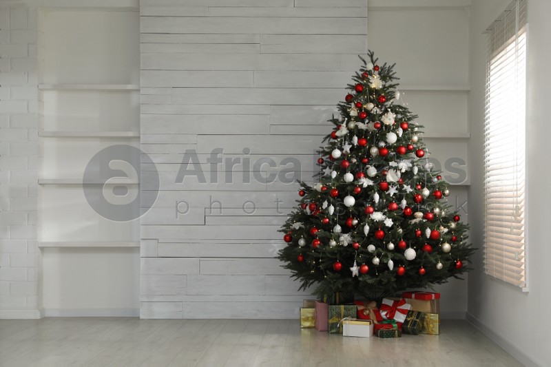 Beautifully decorated Christmas tree and gifts near window in empty room, space for text