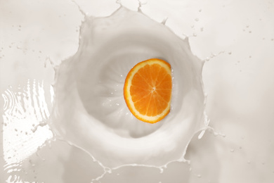 Slice of orange falling in milk with splash, top view