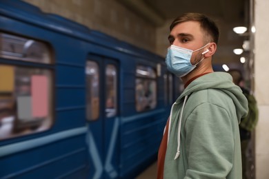 Young man in protective mask at subway station, space for text. Public transport