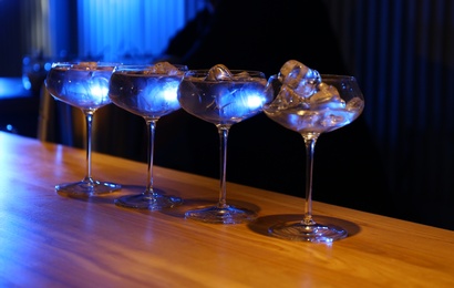 Glasses of vodka with ice cubes on wooden counter in bar