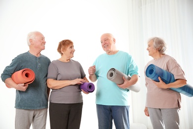 Elderly people with yoga mats on light background