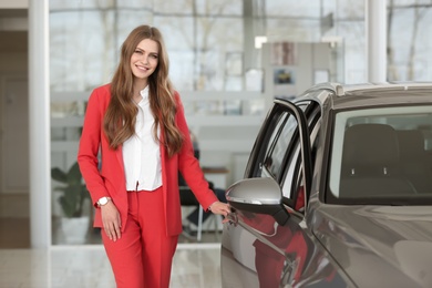 Young saleswoman near automobile in car dealership