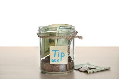 Tip jar and money on wooden table against white background