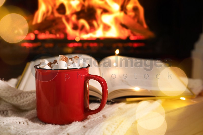 Cup of cocoa and book on wooden table near fireplace. Cozy Christmas atmosphere