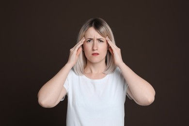 Woman suffering from headache on dark brown background