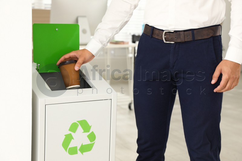 Young man throwing coffee cup into recycling bin in office, closeup