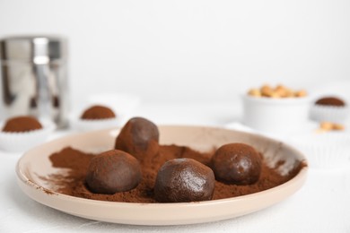 Plate with delicious chocolate truffles and cocoa powder on white table, closeup. Space for text