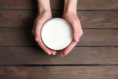 Woman holding glass of milk at wooden table, top view
