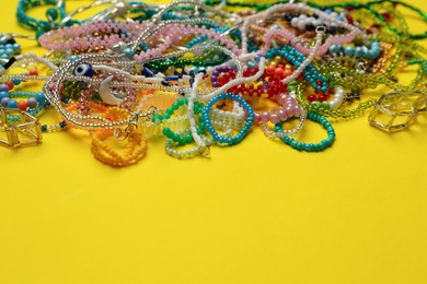 Pile of beautiful handmade beaded jewelry on yellow background. Space for text
