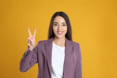 Woman in violet blazer showing number two with her hand on yellow background