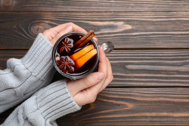 Woman with cup of mulled wine at wooden table, top view. Space for text