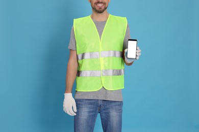 Photo of Male industrial engineer in uniform with phone on light blue background, closeup