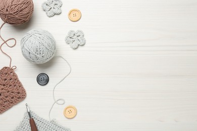 Flat lay composition with knitting threads and crochet hook on white wooden table, space for text