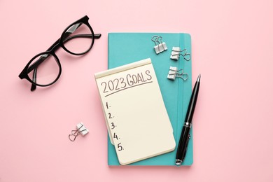 Notebook with inscription 2023 Goals, pen and glasses on pink background, flat lay. New Year aims