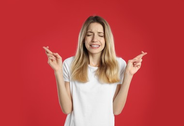 Woman with crossed fingers on red background. Superstition concept