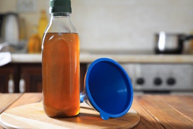 Photo of Bottle with used cooking oil and funnel on wooden table in kitchen
