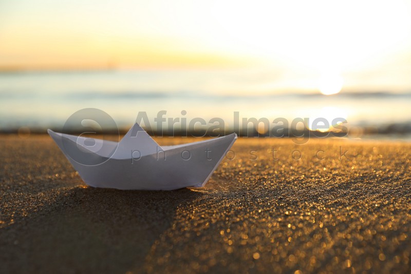 White paper boat on sand near sea at sunset. Space for text