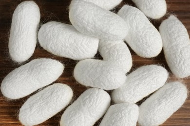 Heap of white silk cocoons on wooden table, flat lay