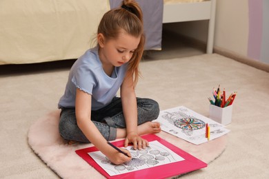 Little girl coloring antistress page on floor indoors