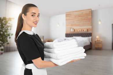 Beautiful chambermaid with clean folded towels in hotel room